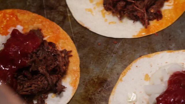 The footage shows a corn tortilla topped with slow-cooked shredded beef (birria), fresh diced white onions, and a generous layer of vibrant red salsa.