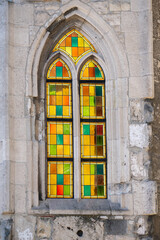Obraz premium Colorful stained glass window set in a Gothic stone frame, highlighting geometric patterns, weathered masonry and historic architectural detail.