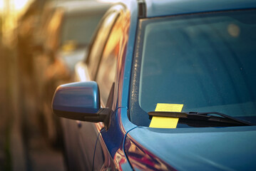 Yellow parking ticket over car windscreen wiper. Payment notice for parking penalty secured under...