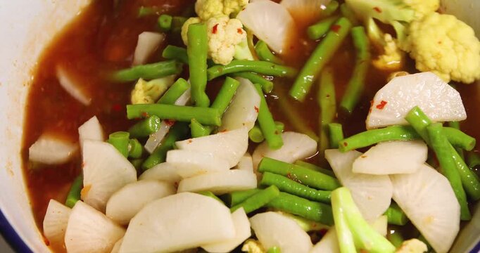Ladle stirring cauliflower, yardlong beans, and Thai white radish (daikon) in bubbling Thai sour curry (Gaeng Som), vibrant spicy-sour broth, showing cooking process
