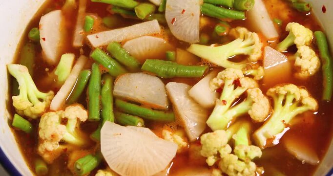 Thai white radish (daikon), cauliflower, and yardlong beans boiling in Thai sour curry (Gaeng Som), bubbling spicy-sour broth, showing cooking process