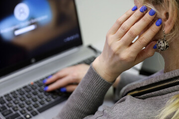Woman in grey blouse working on the laptop keyboard sitting at table. Female hands with blue manicure