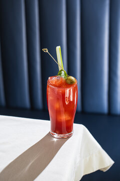 Red bloody mary cocktail with celery olive and ice served in tall glass on table in bar interior
