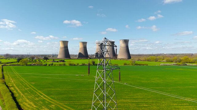 Wide view of power lines crossing green fields toward nuclear power station with multiple cooling towers. Energy infrastructure in rural landscape with transmission network and industrial background