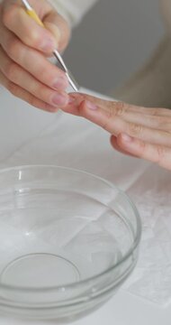 vertical video Woman's hands using a cuticle pusher tool for nail care and hygiene over a bowl of water