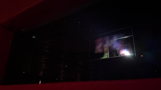 Video of a cinema projector operating inside a movie theater projection room. Light beam shining through the dark hall concept footage.