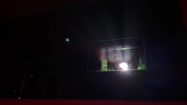 Video of a cinema projector operating inside a movie theater projection room. Light beam shining through the dark hall concept footage.