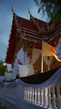 Vertical shot of a traditional Thai Buddhist temple illuminated at dusk with waving flags, Bangkok, Thailand