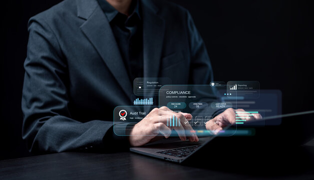 Corporate GRC compliance management and audit readiness dashboard concept. Professional working on laptop with holographic interface showing risk score, regulation controls and audit trail monitoring.