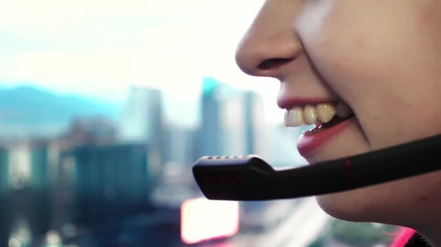 Side profile of female agent speaking beside window with city skyline blurred. Remote consultant is taking client call from highrise workspace wearing headset microphone near mouth. Distant job theme.