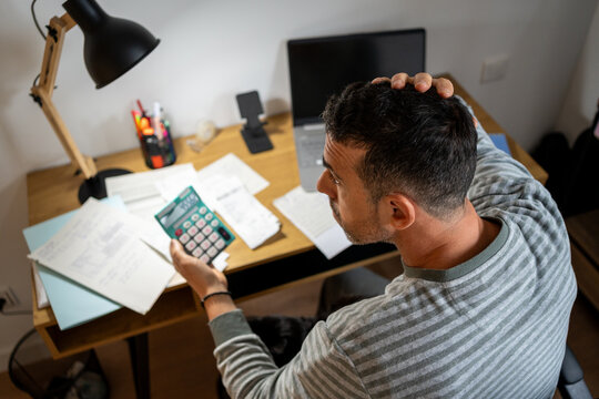 Man calculating finances with calculator, stressing over bills and debts