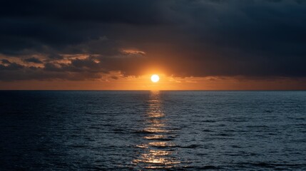 Fototapeta premium Sunset over calm ocean waters with dark clouds and golden reflections creating a serene coastal landscape at dusk, horizon visible in the distance