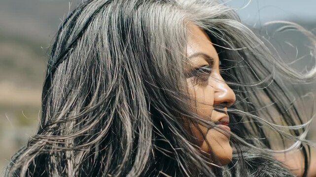 Portrait of a mature woman with flowing silver hair gazing thoughtfully into the distance against a blurred natural landscape backdrop a symbol of wisdom and resilience