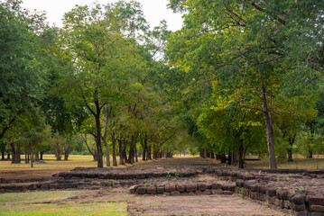 Fototapeta premium Ancient brick ruins at Khao Khlang Nok in Thailand, a historic archaeological site surrounded by trees under a blue sky with clouds