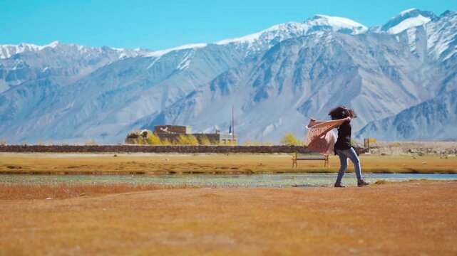 Young beautiful girl spinning on meadow with her arms raised, spins and enjoys the beautiful summer mountain landscapes. Tourist enjoying freedom. Mesmerizing landscape of Zanskar, Ladakh, India.