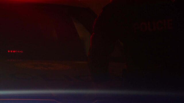 Police officer standing by a patrol car with flashing blue emergency lights at night. Cinematic law enforcement scene with dramatic lighting, lens flares, and tactical atmosphere.
