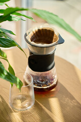 Fresh brewed coffee in filter dripper with empty glass on wooden table in sunlight. Concept of...