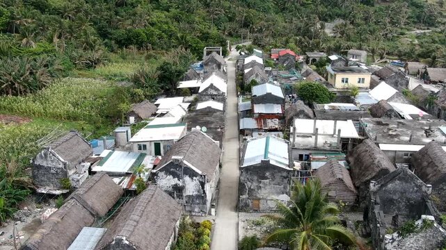 Isometric aerial forward flight over the traditional Ivatan stone houses and thatched roofs of Chavayan Village in Sabtang Island, Batanes, Philippines