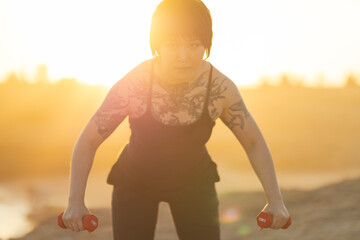 Woman training outdoors holding dumbbells at sunset
