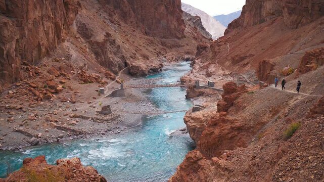 4K shot of beautiful mountain landscape with flowing blue river in Zanskar, Ladakh, India. Hikers hiking on narrow path on cliff. Turquoise blue Tsarap river in rocky Himalaya mountains. Travel and ho