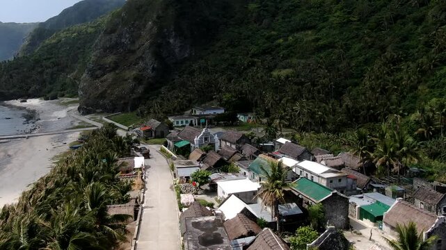 Aerial rising and forward flight over the historic Santa Rosa de Lima stone chapel and traditional Ivatan houses of Chavayan Village in Sabtang Island, Batanes, Philippines