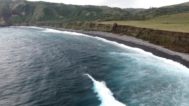 Aerial forward flight over the crashing ocean waves and unique smooth stones of Valugan Boulder Beach in Basco, Batanes, Philippines