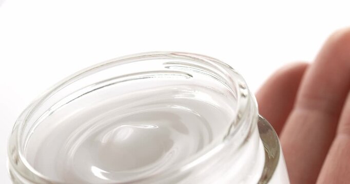 Hand holding an open jar of cosmetic facial cream, close-up footage. Lid is being removed from the jar of cosmetic cream.