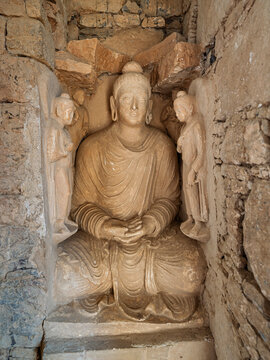 Vertical view of ancient stucco plaster statue of sitting Buddha in meditation in niche of historic Jaulian monastery, Taxila, Khyber Pakhtunkhwa, Pakistan