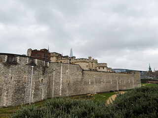 Historic Tower of London fortress and medieval city walls along the River Thames in London, UK under a cloudy sky showcasing stone ramparts and turrets © AS Photo Family