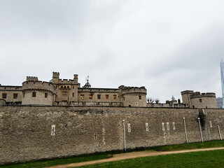 Tower of London historic castle and fortress walls in London, UK with stone battlements, turrets and city skyline under overcast sky © AS Photo Family