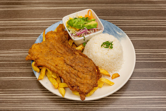 A generous portion of Peruvian-style "bistec a lo pobre," featuring seared steak topped with a light tomato and onion sauce, served with crispy French fries, fluffy rice