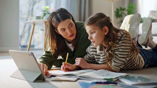 Relaxed babysitter teaching girl online homework on tablet lying floor closeup