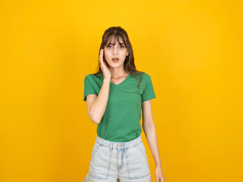 Shocked caucasian woman touching face with hand, reacting with surprise and disbelief concept idea image, wearing green t-shirt, isolated on bright yellow studio background with copy space.
