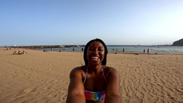 Happy young african american woman smiling on camera during summer beach vacation - UGC content