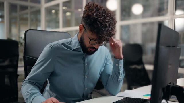 Stressed suffering Arabian business man holding head suffer thinking headache problem deep in thoughts with problem work typing computer at office ethnic businessman male suffer with ache working pc