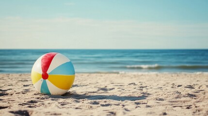 Obraz premium Colorful beach ball rests on sandy shore near calm ocean on a sunny day with clear sky and gentle waves