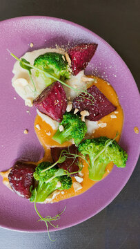 Gourmet vegetarian dish with roasted beetroot, broccoli, and nuts on a purple plate