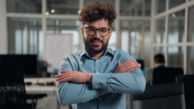 Portrait in office Hindu ethnic business man thinking looking at camera crossed hands pose smiling toothy Arabian businessman think creative male guy executive in glasses smile happy crossing arms