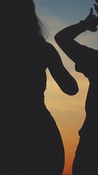 Two women are silhouetted against a sunset. The women appear to be engaged in a moment of candid interaction during the evening.