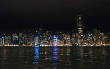 Obraz premium Hong Kong cityscape glows brightly at night over Victoria Harbour, displaying many tall buildings and water reflections