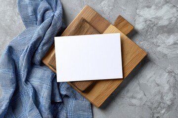 Fototapeta premium Overhead shot Blank card atop two wooden cutting boards, blue cloth, marble surface