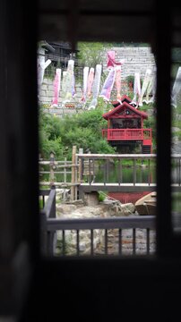 프레임 너머로 보이는 비 내리는 니지모리 스튜디오의 붉은 사당과 고이노보리 (View of red shrine and Koinobori through a frame at Nijimori Studio on a rainy day)