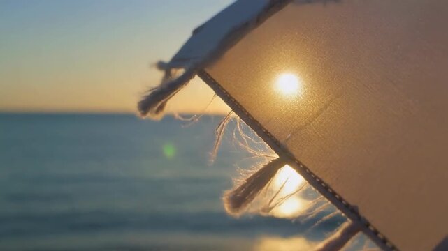 Sunlight filtering through a beach umbrella at sunset with the ocean in the background. 4k Footage Video