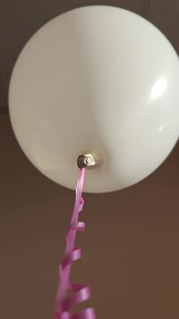White balloon with pink ribbon slowly rising against a neutral background, showcasing the gradual ascent and movement of the decorative element in a festive setting
