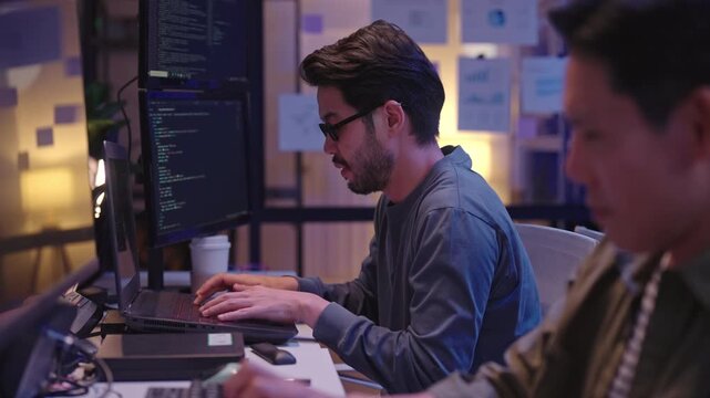 Professional male developer working hard on a software project in a dimly lit office workspace.
