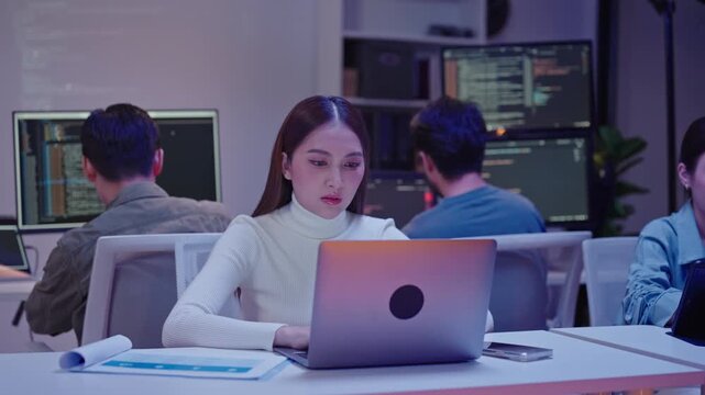 Exhausted woman programmer focusing on her computer screen during a long night of software debugging.