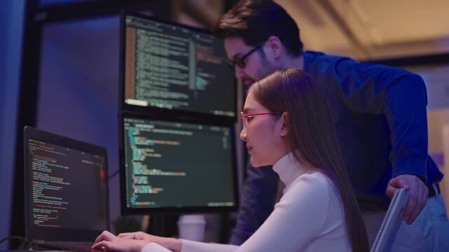 Asian man and woman programmers talking about project issues while working overtime in a modern office.