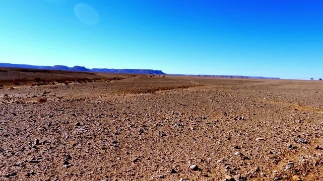 Driving pov on a bumpy dirt road through the vast, arid moroccan desert landscape under a clear blue sky on a sunny day