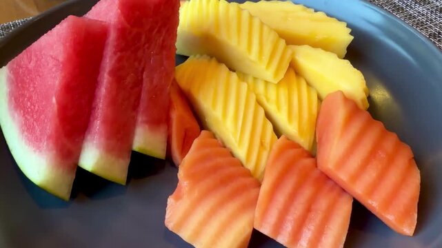 Freshly sliced tropical fruit platter on a blue ceramic plate featuring juicy watermelon, sweet pineapple, and ripe papaya. Healthy organic breakfast served in a hotel during summer vacation.