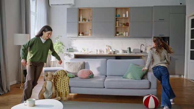 Parent daughter playing home running around sofa. Excited mom catching girl